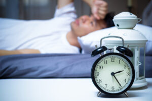 man in bed with alarm clock next to him 